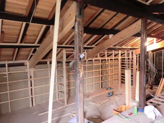 天井板の施工中、古い梁と新しい杉板が見える室内