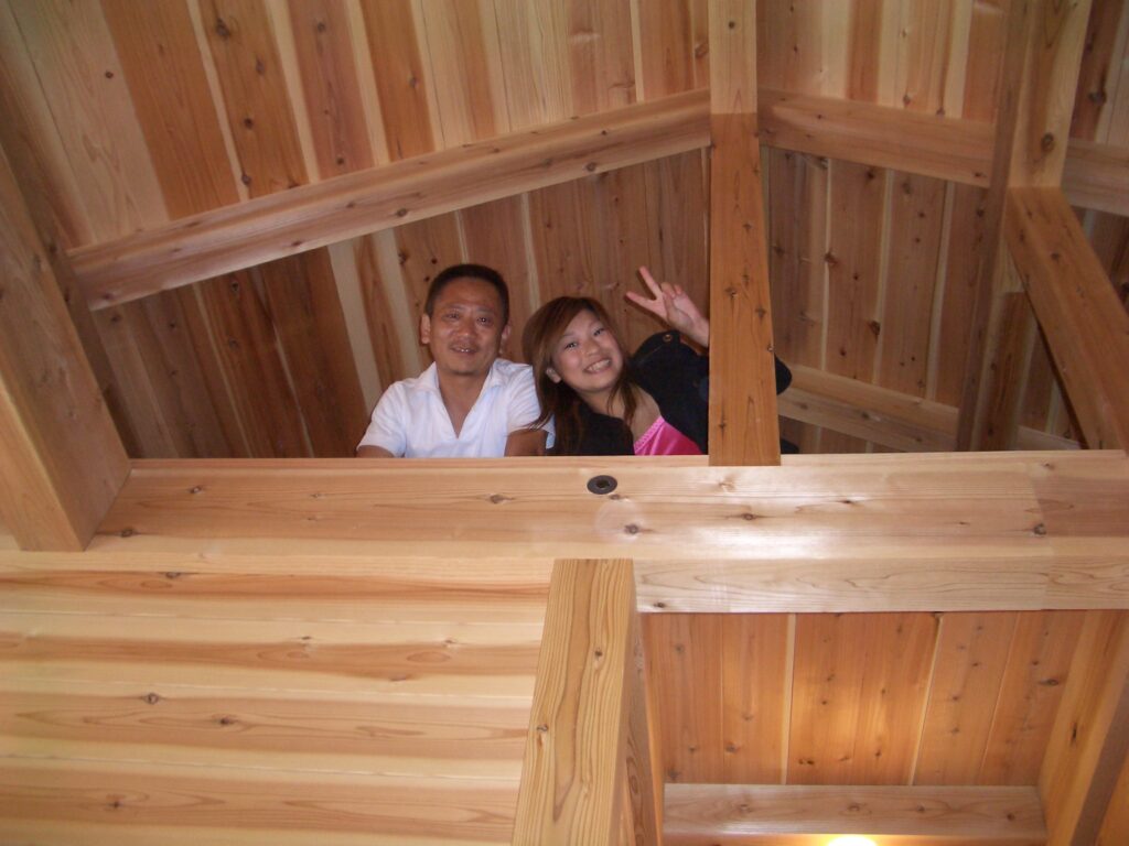 ロフトから笑顔で手を振るご夫婦。杉板の壁に囲まれた開放的な空間