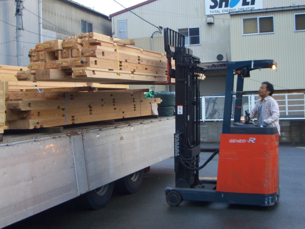 フォークリフトでトレーラーから板倉造り用の杉材を降ろす様子