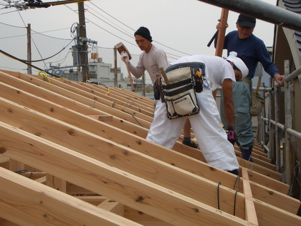 上棟時に大工が小屋組みの上で屋根の野地板を施工している様子