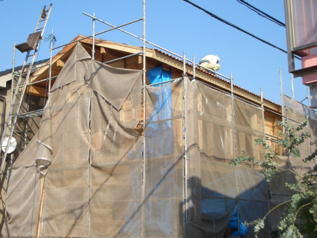 屋根工事中の外観。足場と養生シートに覆われた建物