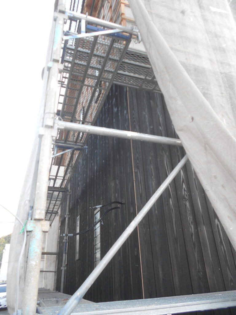 足場の中で黒い焼杉が施工された外壁の様子