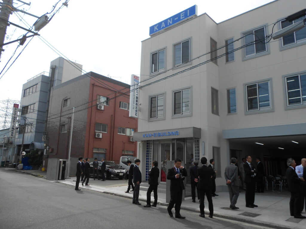 竣工した鉄骨造3階建て事務所ビルの外観と竣工式の参加者