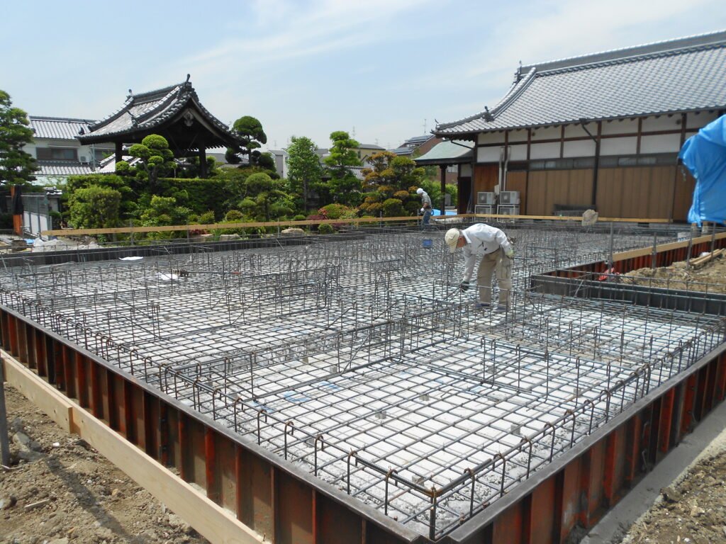 お寺の庫裏の基礎配筋検査の様子、寺院の本堂を背景に