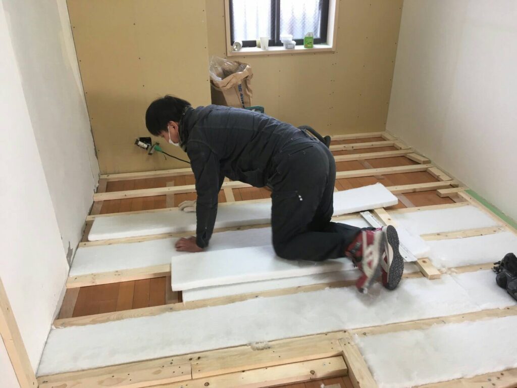 床下地の根太の間に断熱材を敷き込む作業